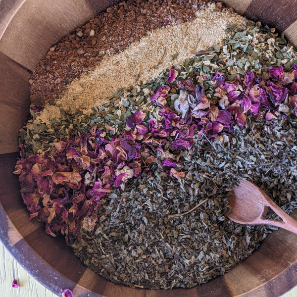 crushed hawthorn berries, crushed ginger, hawthorn leaves and flowers, rose petals and lemon balm herbs in a bowl with spoon